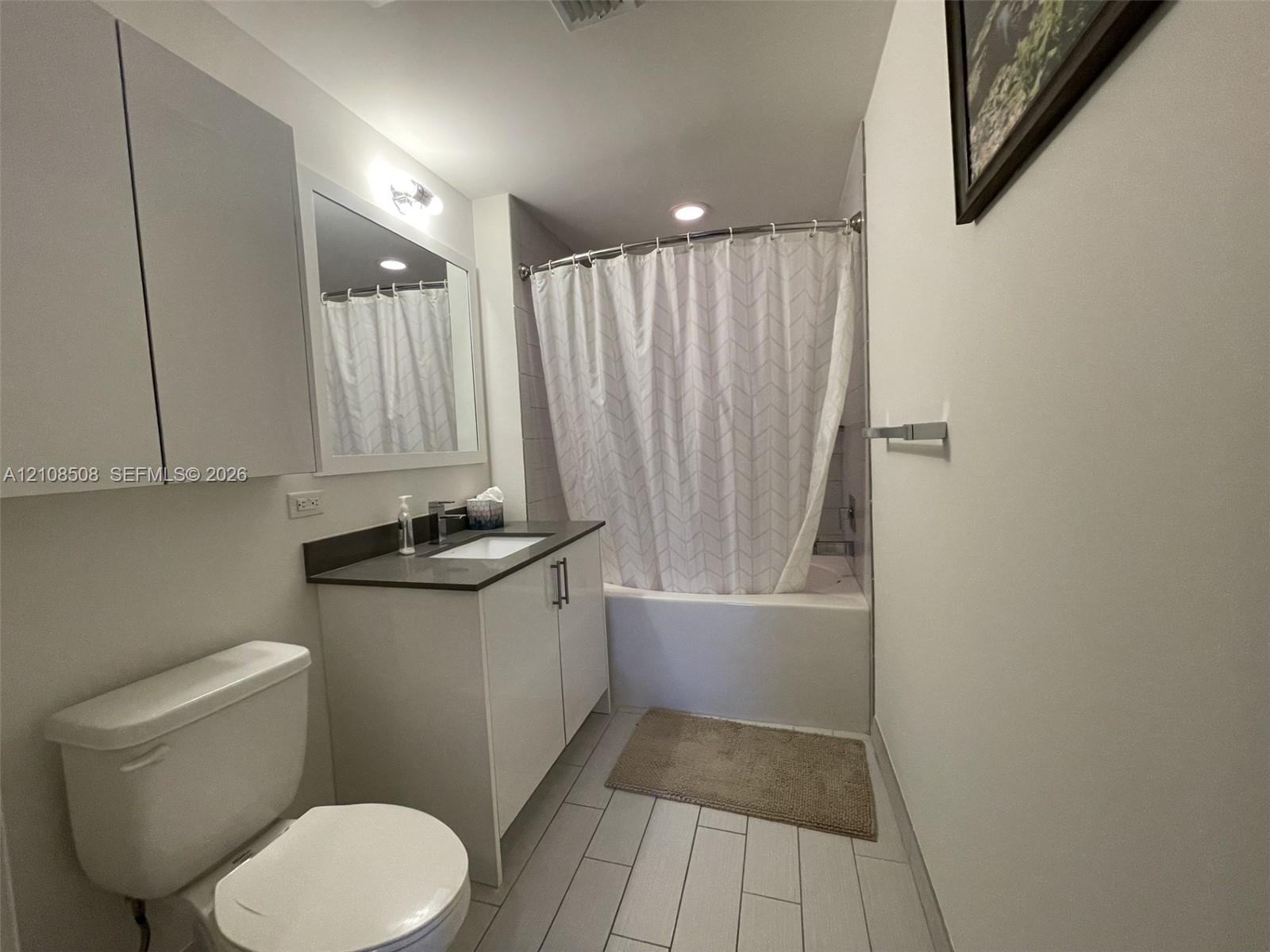 Bathroom featuring a vanity with dark countertop, rectangular integrated sink, tall storage cabinetry, and a bathtub with tile surround