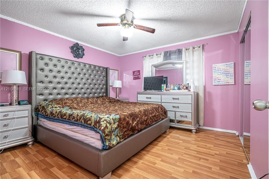 Bedroom interior featuring wood-finish flooring, a ceiling fan with light fixture, and a sliding-door closet Bedroom interior featuring wood-finish flooring, a ceiling fan with light fixture, and a sliding-door closet