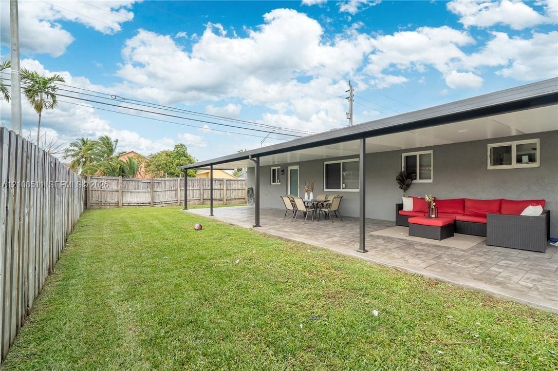 Expansive backyard featuring a manicured lawn, a paved patio, a full-length covered terrace, and perimeter wood fencing