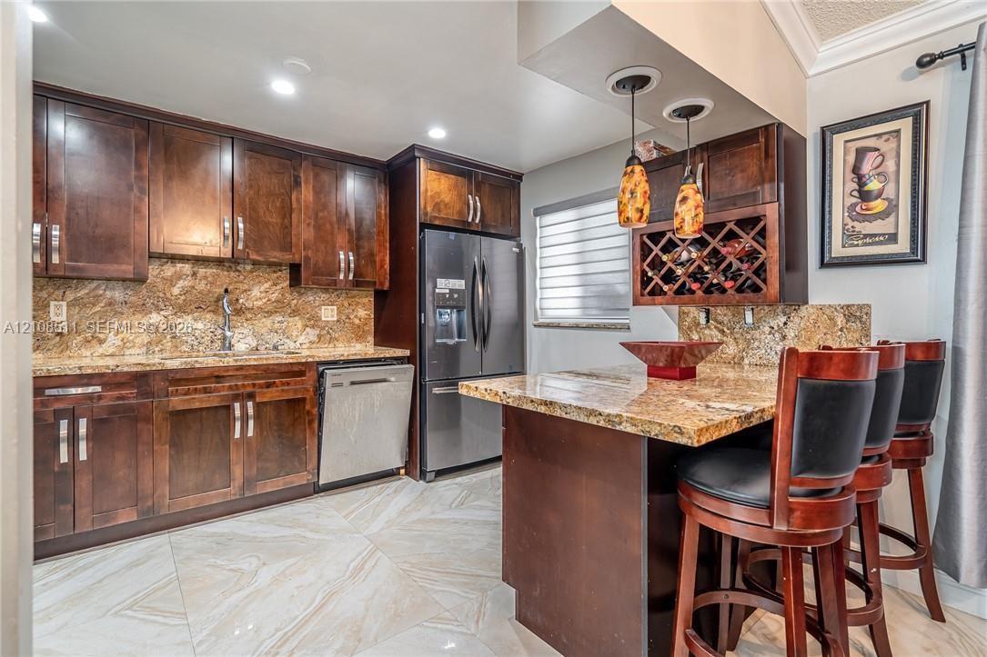 Kitchen featuring dark wood cabinetry, natural stone countertops, a built-in wine rack, dual pendant lighting, and large-format tile flooring