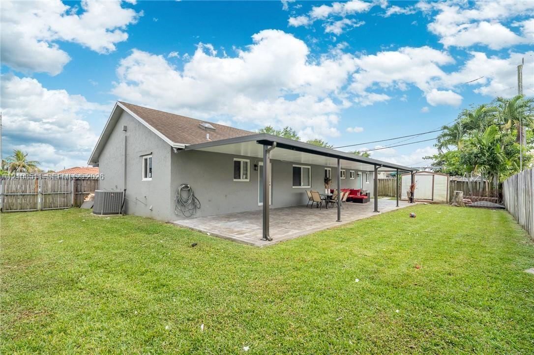 Spacious backyard featuring a covered patio, paved hardscaping, wood-style privacy fencing, and exterior storage structure