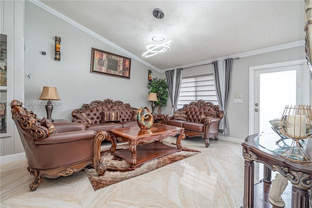 Living area featuring polished tile flooring, contemporary multi-ring LED light fixture, and crown molding