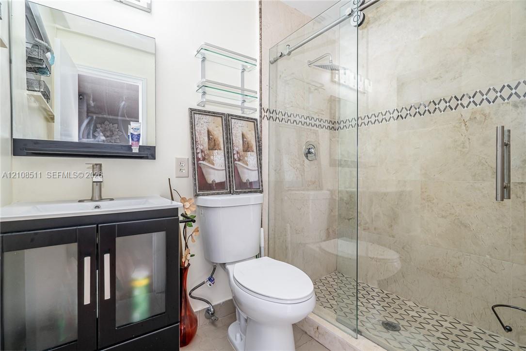 Bathroom featuring a vanity with frosted glass cabinet doors, a rectangular sink, a shower enclosure with sliding glass doors, stone wall tile, and a geometric patterned tile shower floor Bathroom featuring a vanity with frosted glass cabinet doors, a rectangular sink, a shower enclosure with sliding glass doors, stone wall tile, and a geometric patterned tile shower floor