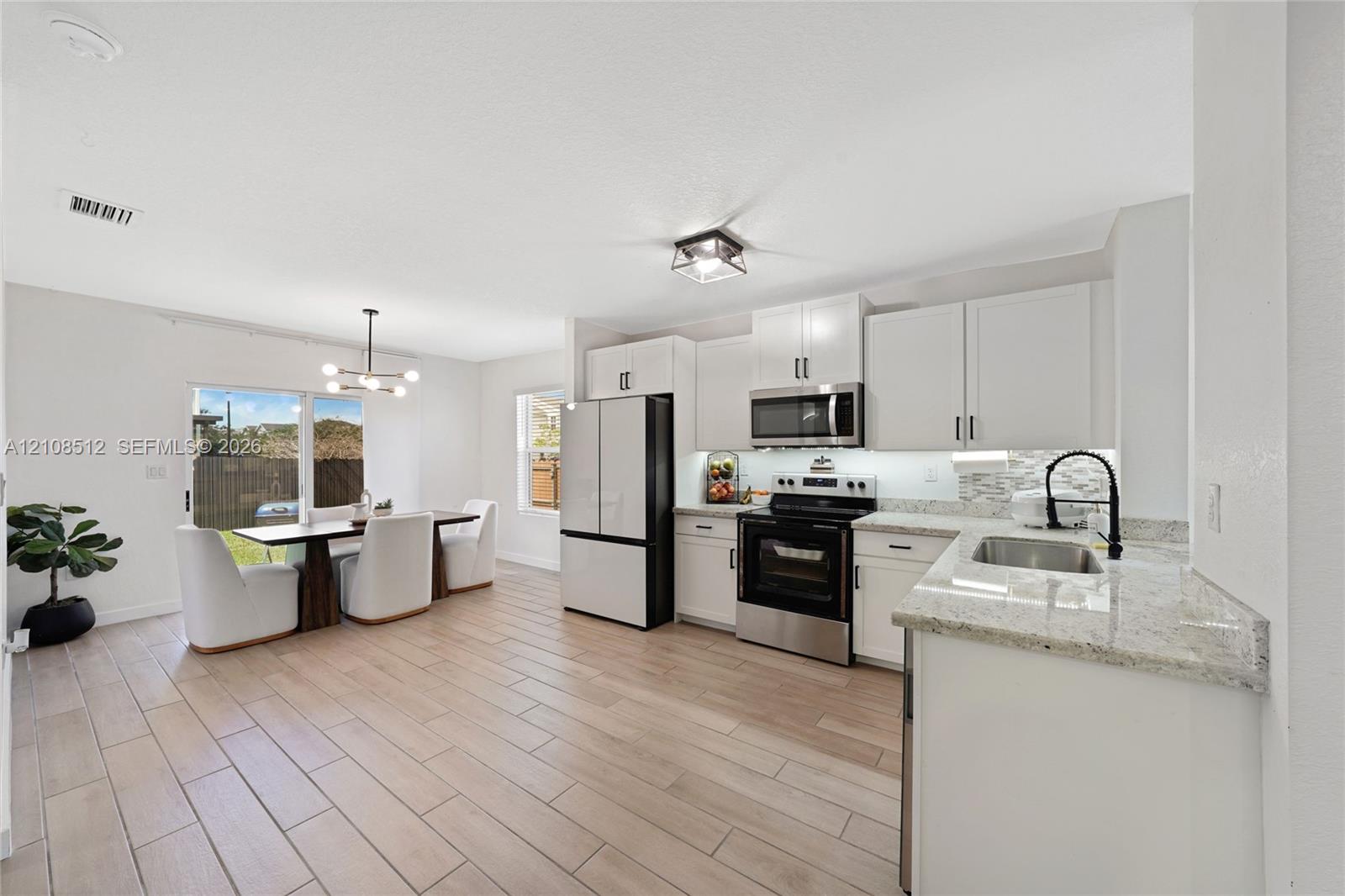 Kitchen featuring white shaker-style cabinetry, stone-finish countertops, stainless steel appliances, wood-finish tile flooring, and a multi-light fixture