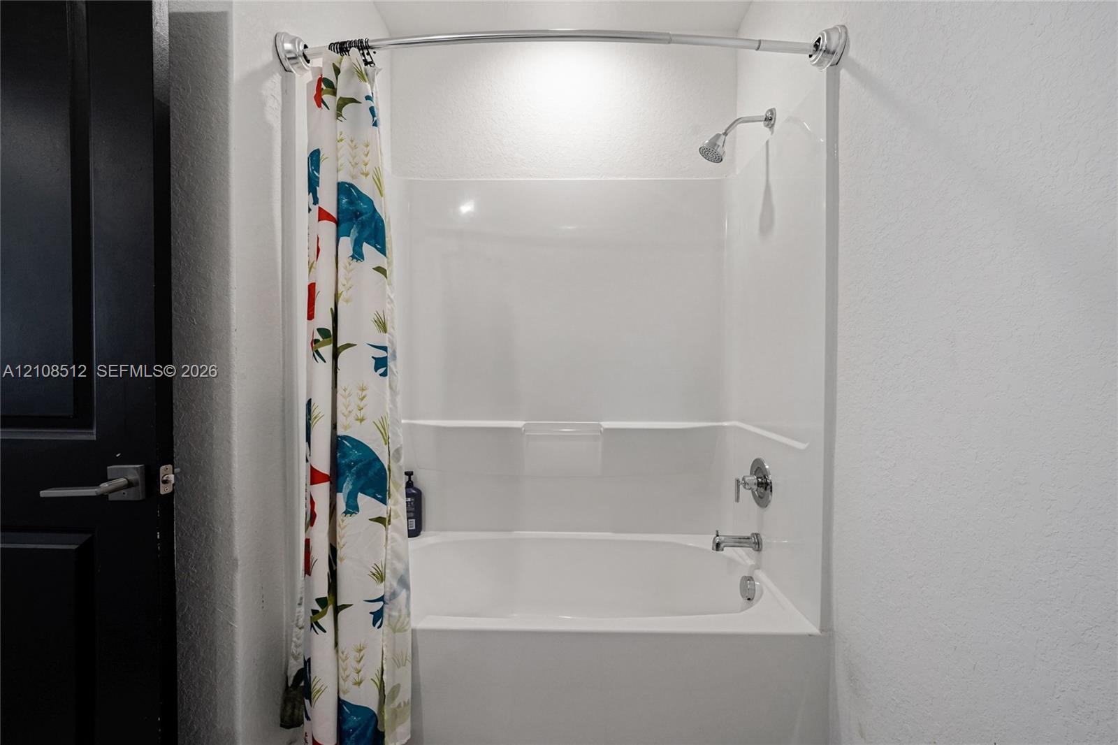 Bathtub and shower combination with a white acrylic surround, integrated shelving, a polished chrome faucet, and a wall-mounted shower head