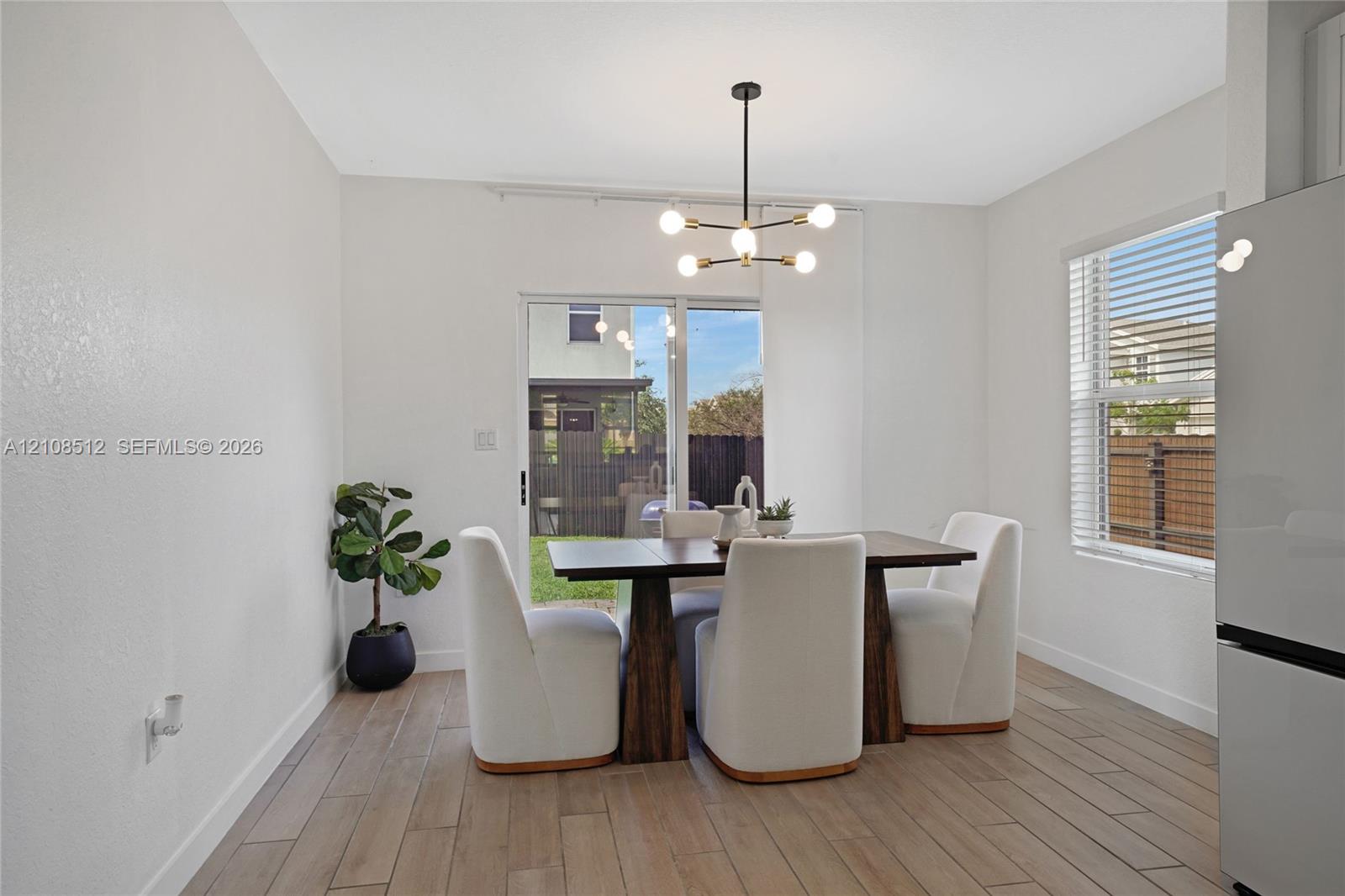 Dining area featuring wood-finish flooring, a modern six-light chandelier, a large window, and a sliding glass door providing external access