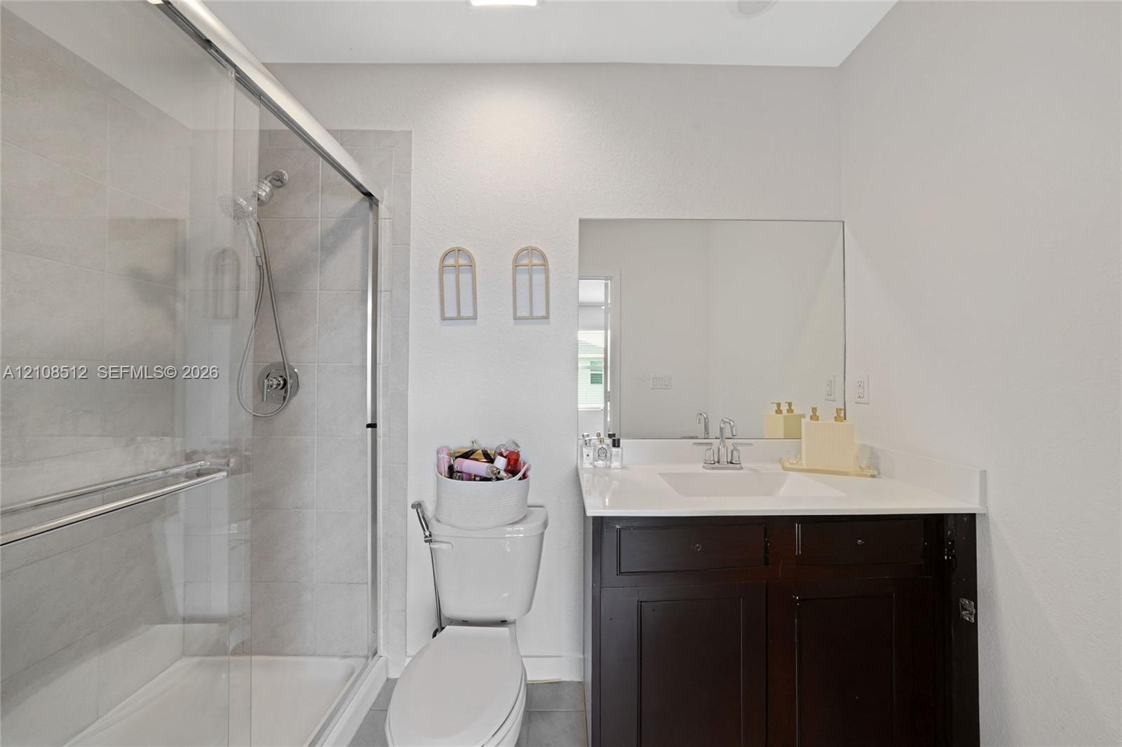 Bathroom featuring a dark wood-finish vanity with a stone countertop, an integrated rectangular sink, a glass-enclosed shower with tiled surround, and a large wall-mounted mirror