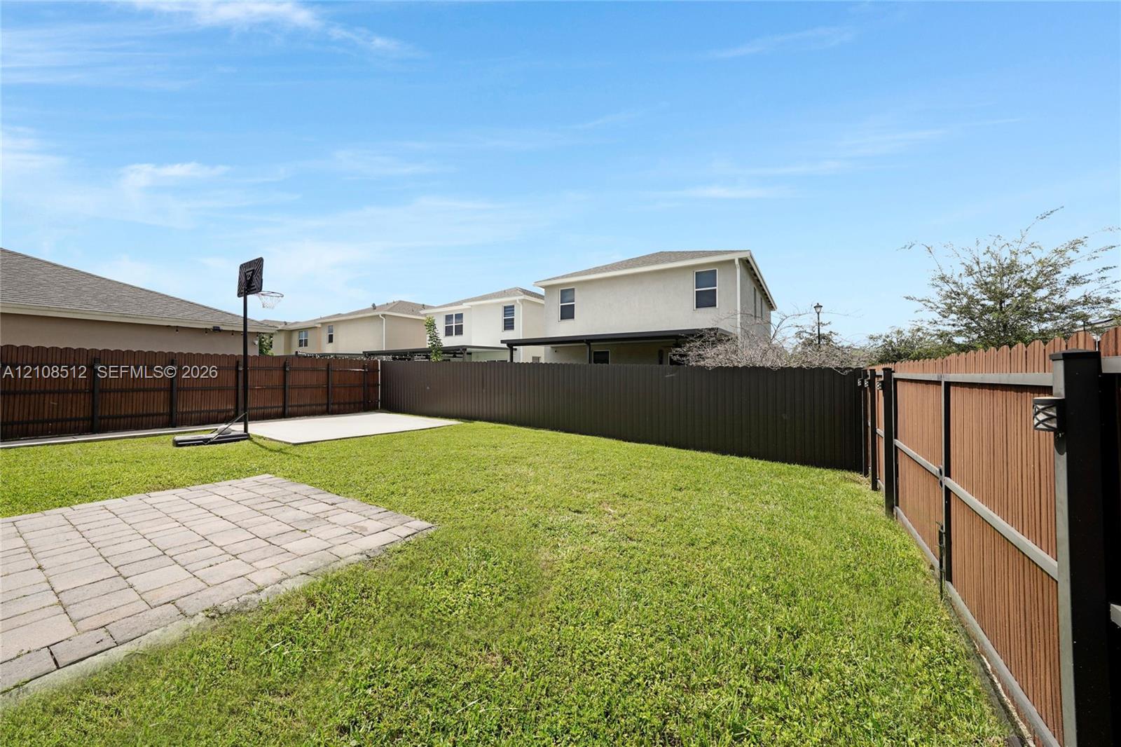 Fenced backyard featuring a manicured lawn, concrete patio, and a dedicated concrete play area