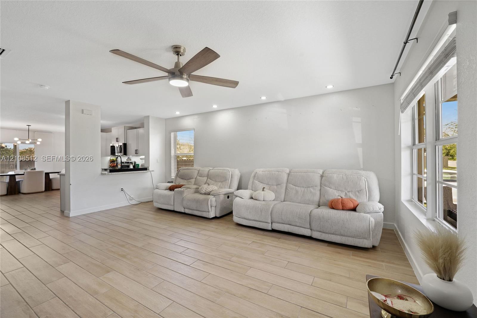 Open-concept area featuring wood-finish tile flooring, recessed lighting, a modern ceiling fan with integrated lighting, and expansive windows