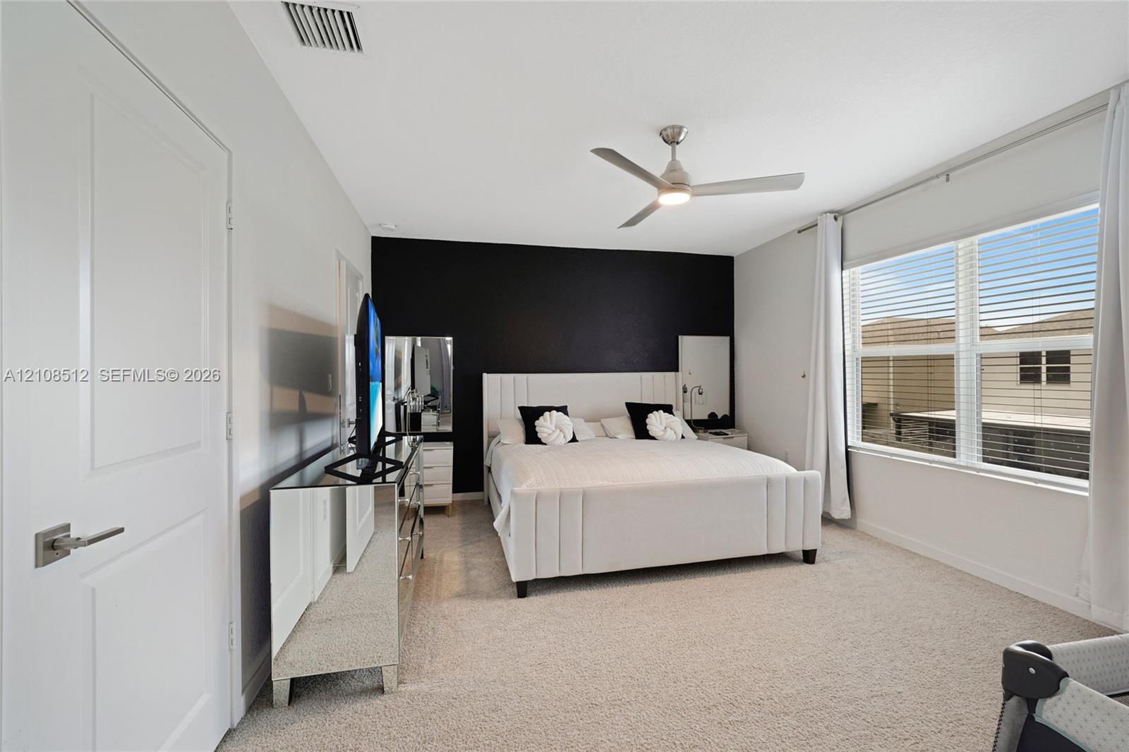 Bedroom featuring neutral carpeting, a high-contrast accent wall, and a multi-blade ceiling fan with integrated lighting Bedroom featuring neutral carpeting, a high-contrast accent wall, and a multi-blade ceiling fan with integrated lighting