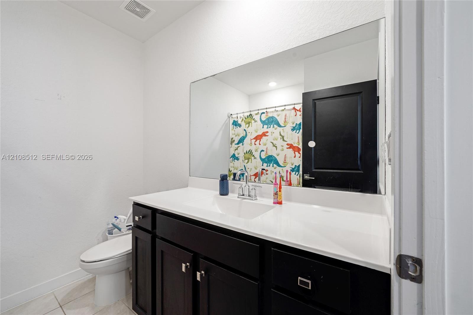 Dark-finish vanity cabinetry with a white integrated countertop, large wall-mounted mirror, and black-painted interior door