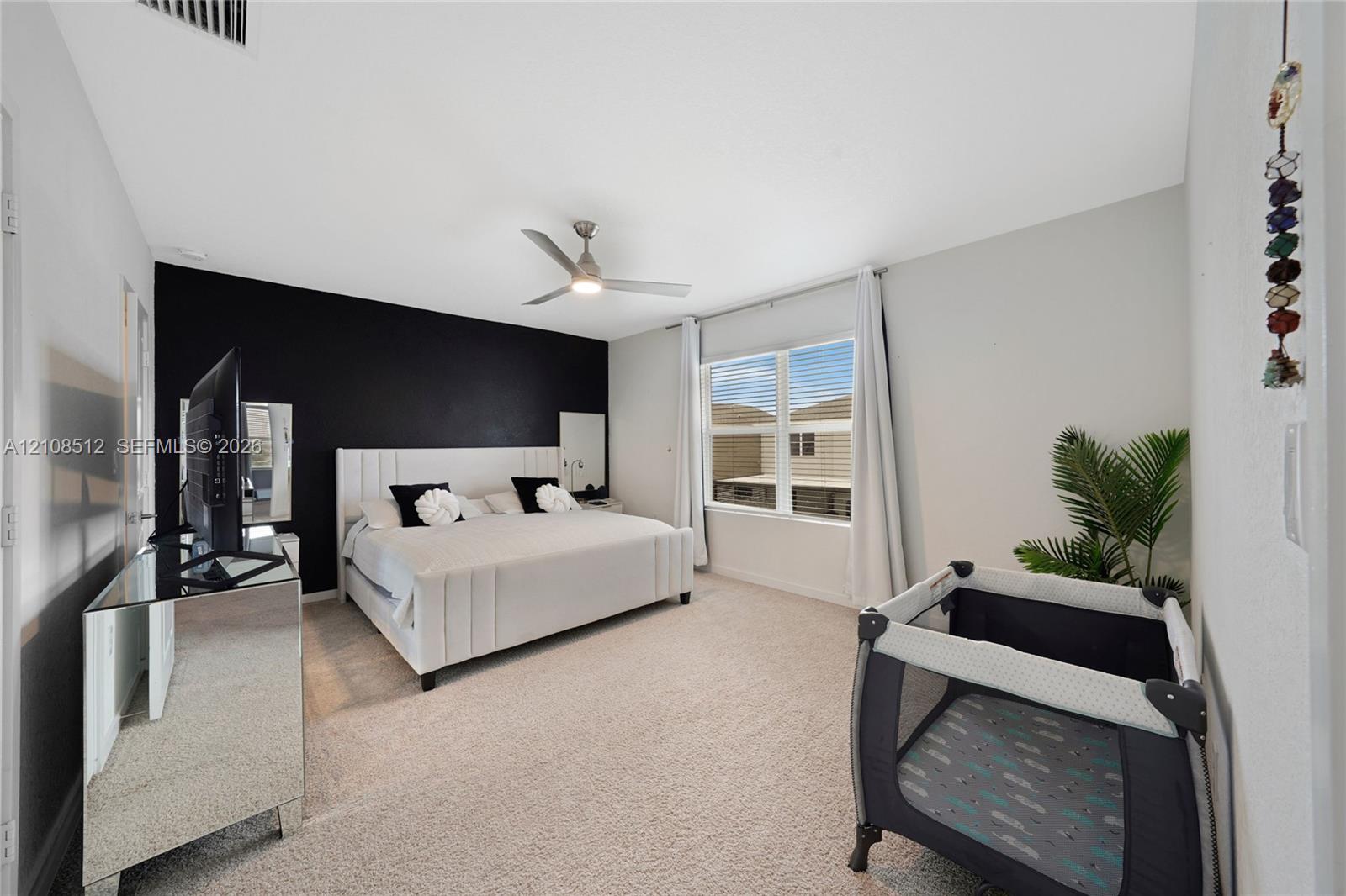 Bedroom featuring vaulted ceilings, a prominent accent wall, neutral carpeting, and a ceiling fan with integrated lighting Bedroom featuring vaulted ceilings, a prominent accent wall, neutral carpeting, and a ceiling fan with integrated lighting