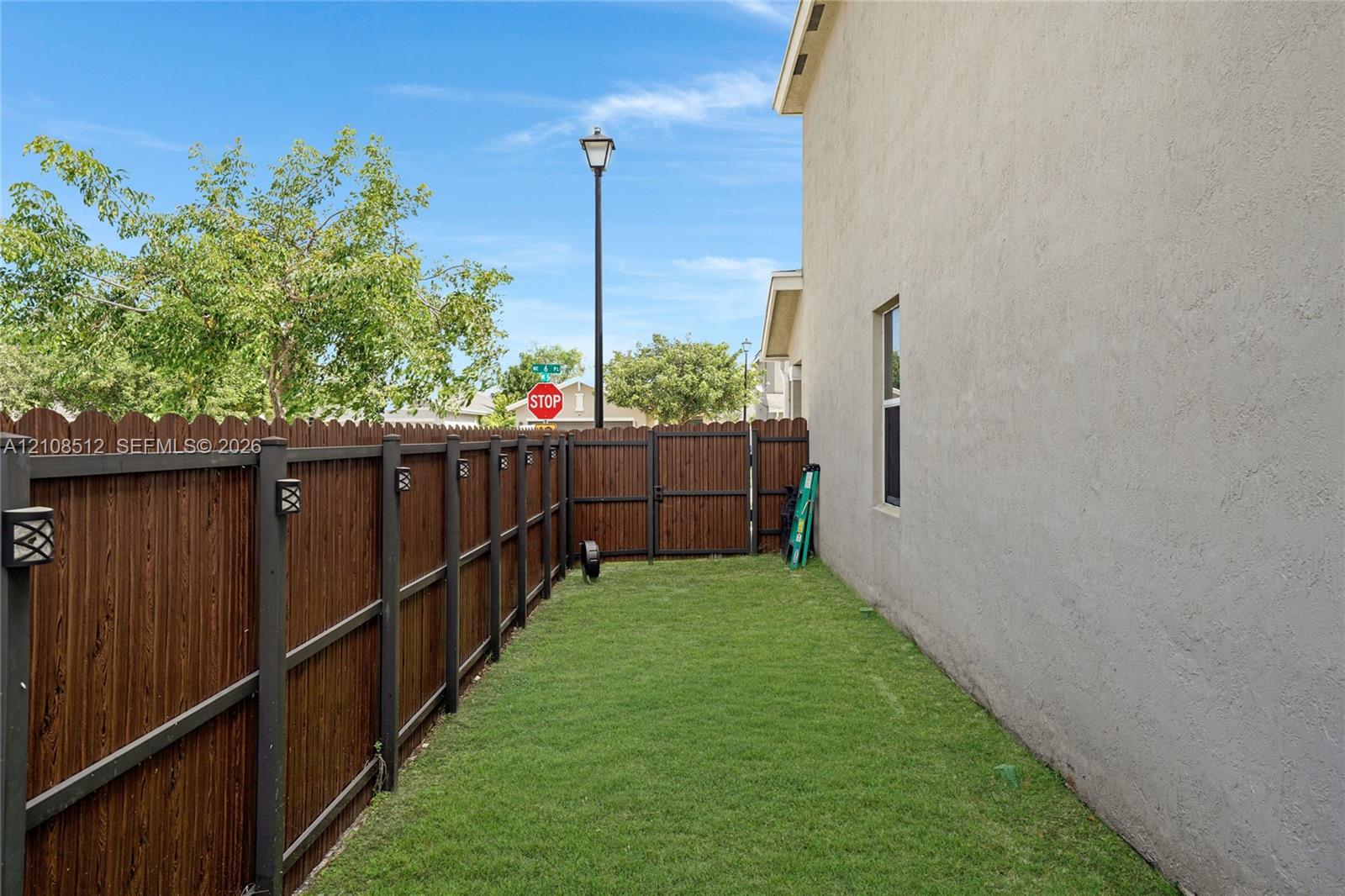 Stucco exterior wall with a private wood-style privacy fence, integrated post lighting, and a manicured grass lawn