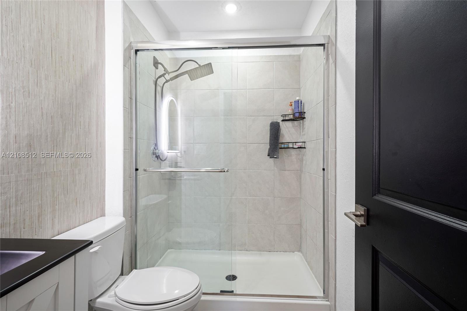Walk-in shower featuring glass sliding doors, neutral ceramic tile surround, and a rain-style showerhead, complemented by a matte black interior door with matching hardware