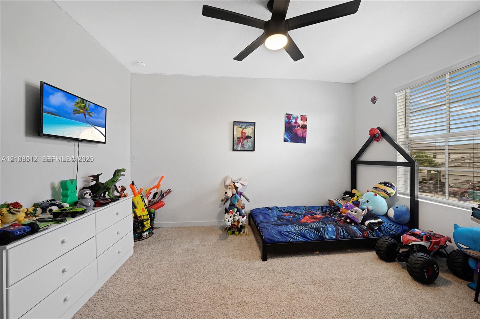 Neutral-toned interior space featuring wall-to-wall carpeting, a multi-blade ceiling fan with integrated lighting, and a large window with horizontal blinds Neutral-toned interior space featuring wall-to-wall carpeting, a multi-blade ceiling fan with integrated lighting, and a large window with horizontal blinds