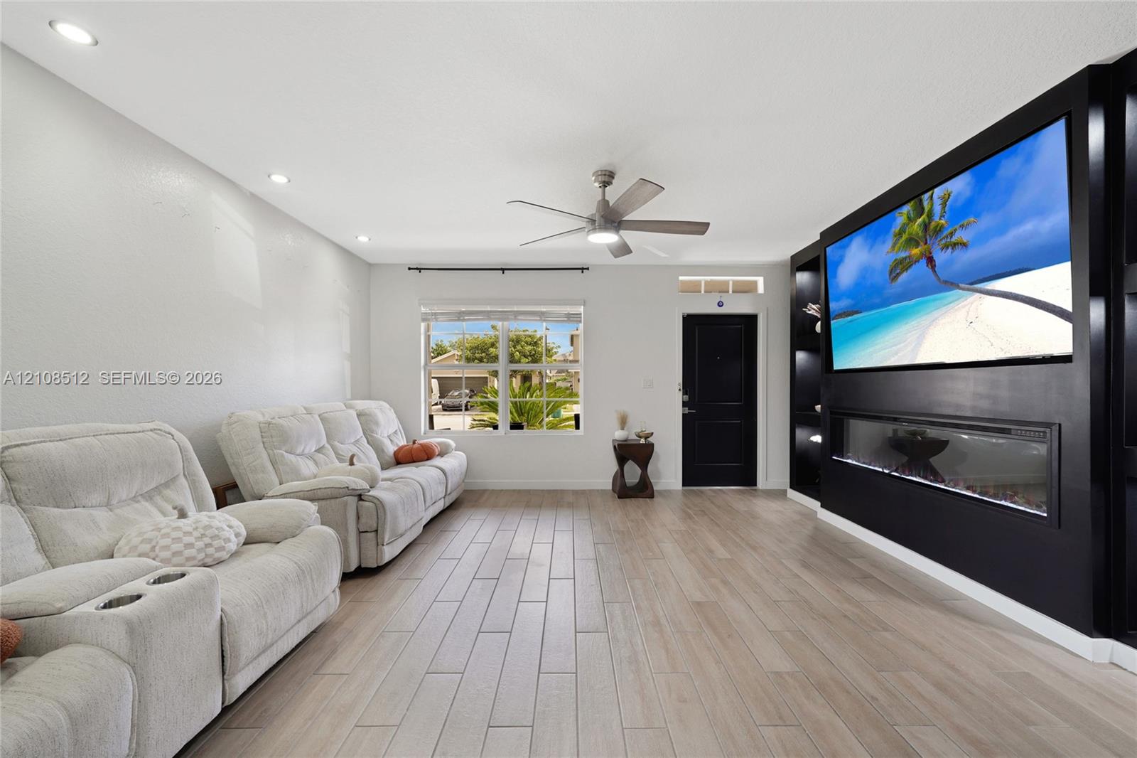 Living area featuring wood-finish flooring, recessed lighting, a modern ceiling fan, and a built-in media wall with a linear electric fireplace
