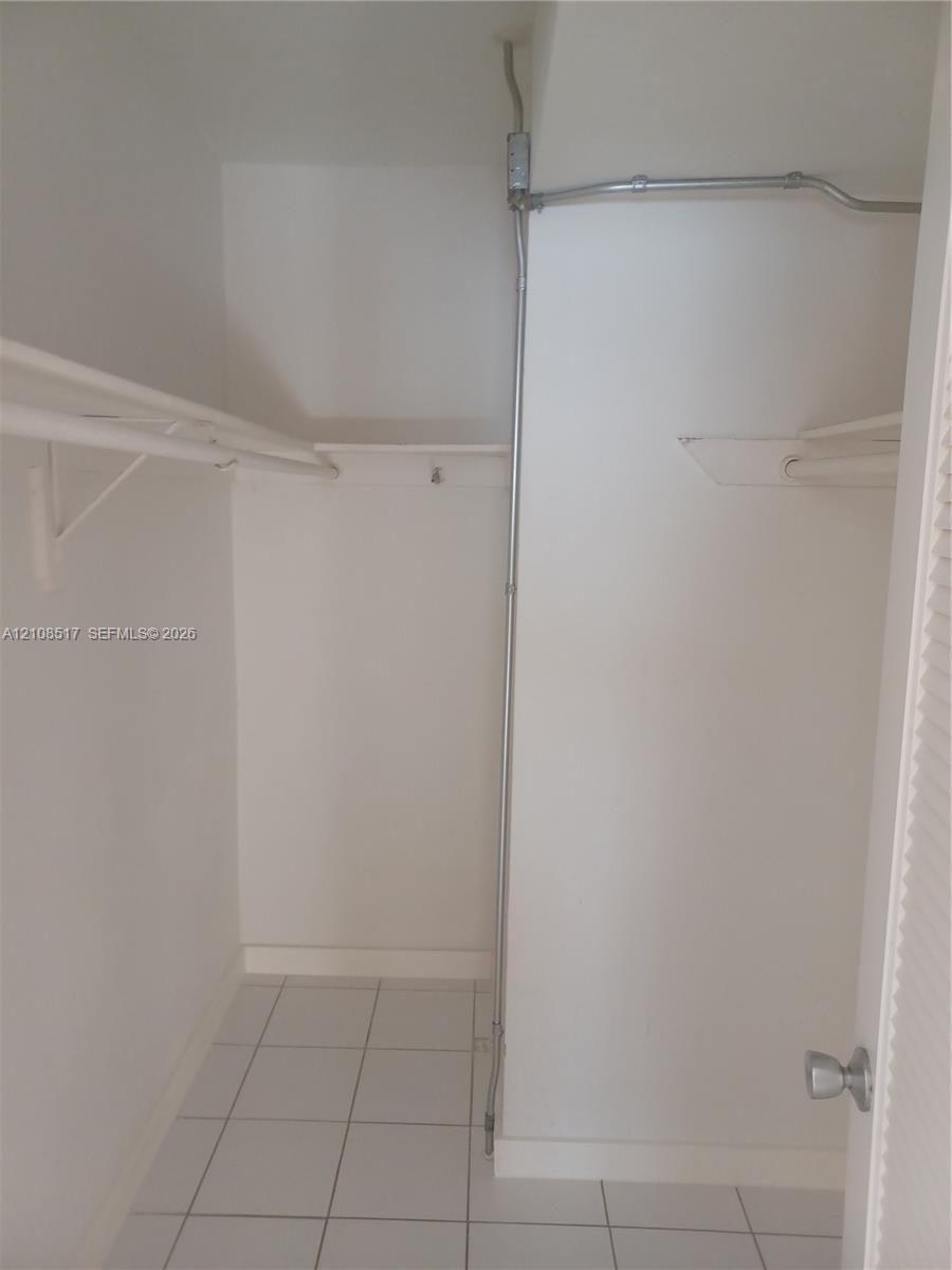 Storage area featuring white tile flooring, built-in metal shelving, and a louvered door Storage area featuring white tile flooring, built-in metal shelving, and a louvered door