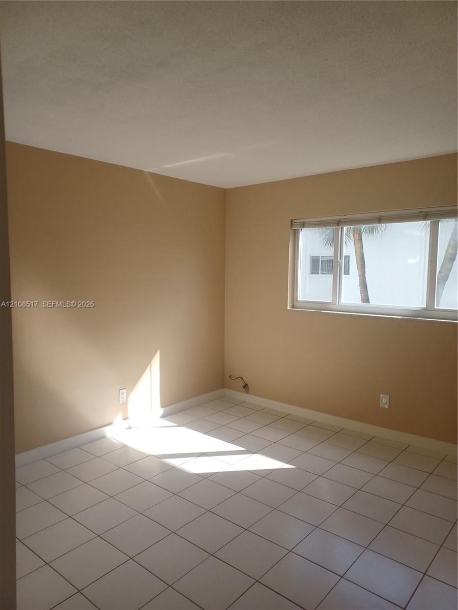Neutral-toned interior space featuring light-colored ceramic tile flooring, horizontal window blinds, and natural light exposure Neutral-toned interior space featuring light-colored ceramic tile flooring, horizontal window blinds, and natural light exposure