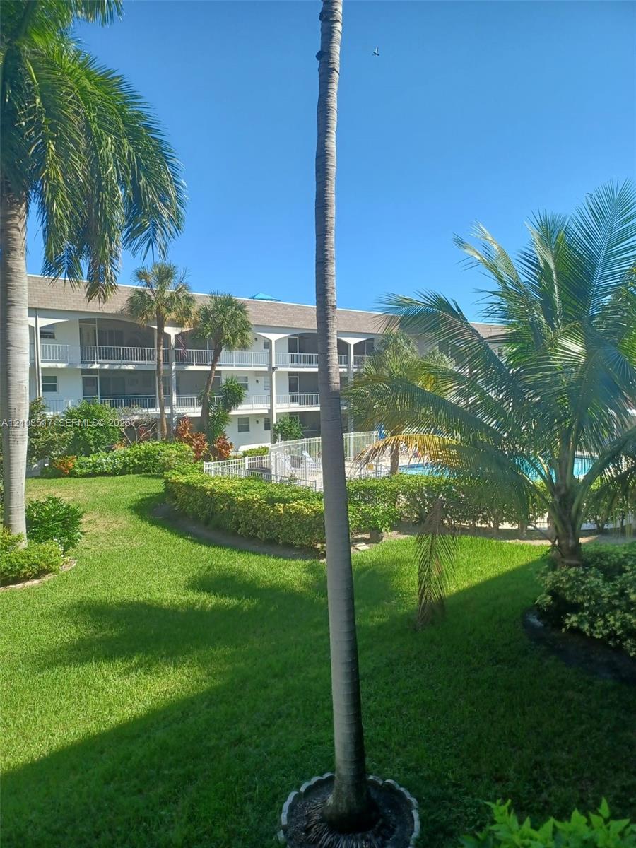 Multi-story building featuring tiered balconies, expansive green space, manicured landscaping, mature palm trees, and an exterior swimming pool