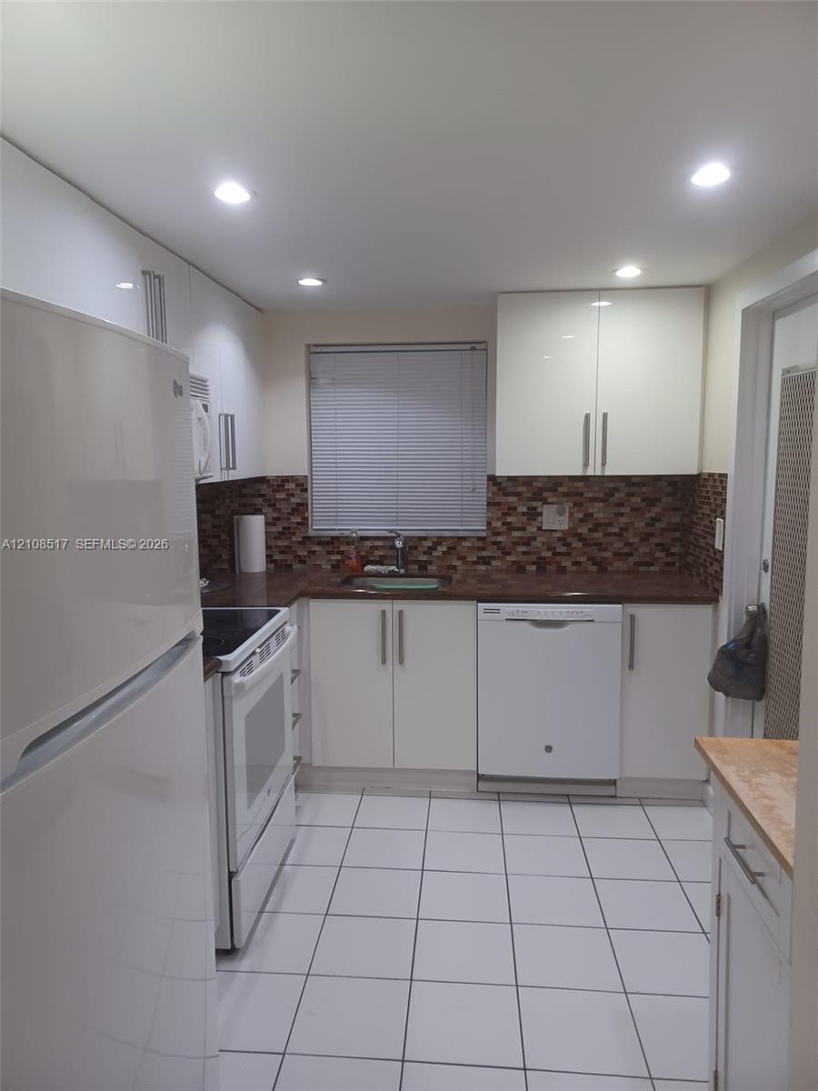 Kitchen featuring high-gloss white cabinetry, white ceramic tile flooring, a mosaic tile backsplash, and recessed ceiling lighting Kitchen featuring high-gloss white cabinetry, white ceramic tile flooring, a mosaic tile backsplash, and recessed ceiling lighting