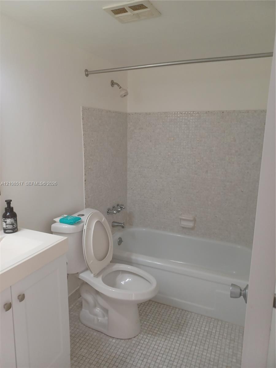 Bathroom featuring a white vanity cabinet with a countertop basin, a porcelain soaking tub, and tile wall surround with matching mosaic floor tiling Bathroom featuring a white vanity cabinet with a countertop basin, a porcelain soaking tub, and tile wall surround with matching mosaic floor tiling