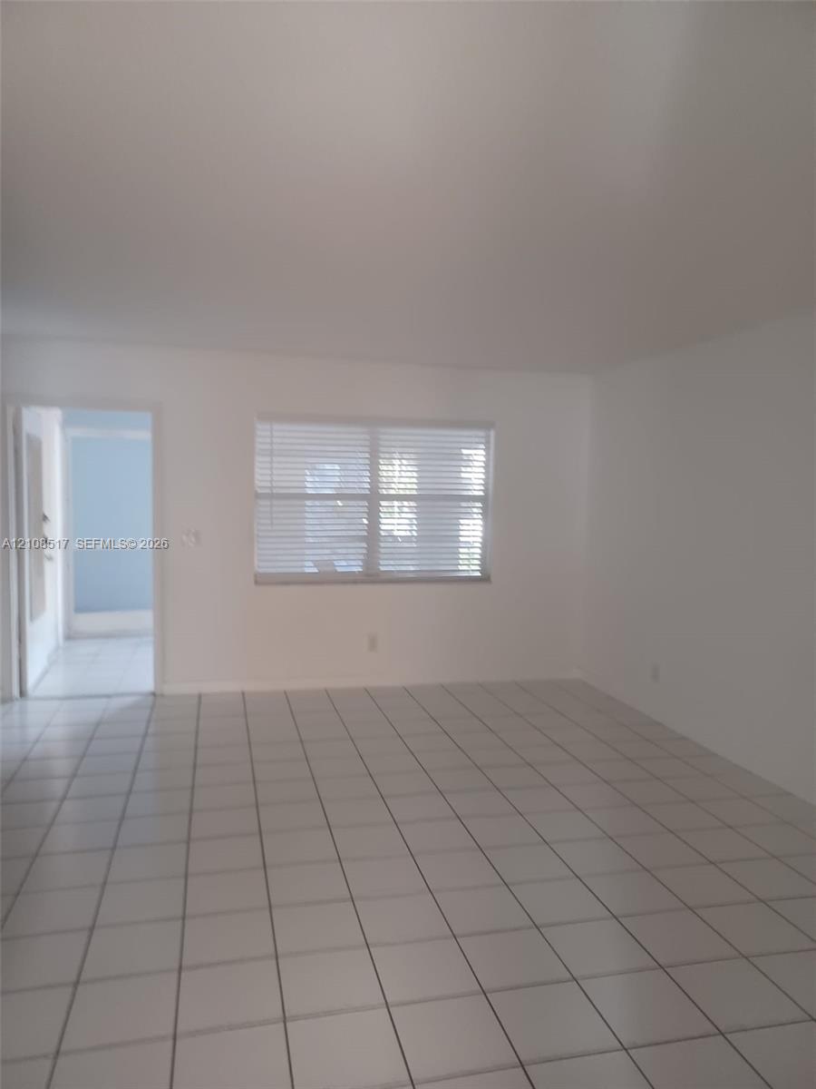 Neutral-toned interior space featuring white walls, large-format ceramic tile flooring, and a multi-pane window with horizontal blinds Neutral-toned interior space featuring white walls, large-format ceramic tile flooring, and a multi-pane window with horizontal blinds