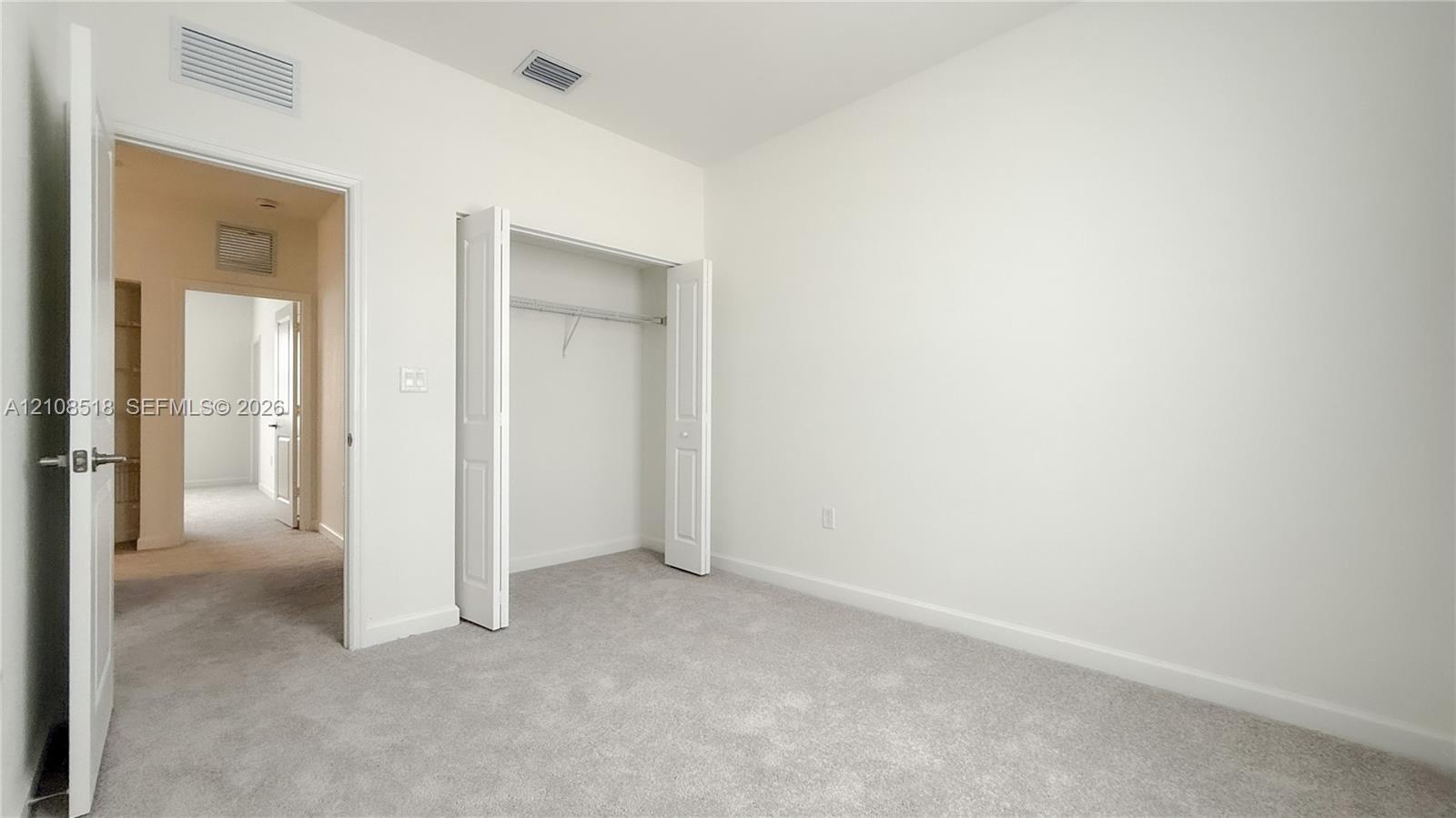 Neutral-toned wall paint, wall-to-wall carpeting, and a bi-fold door closet