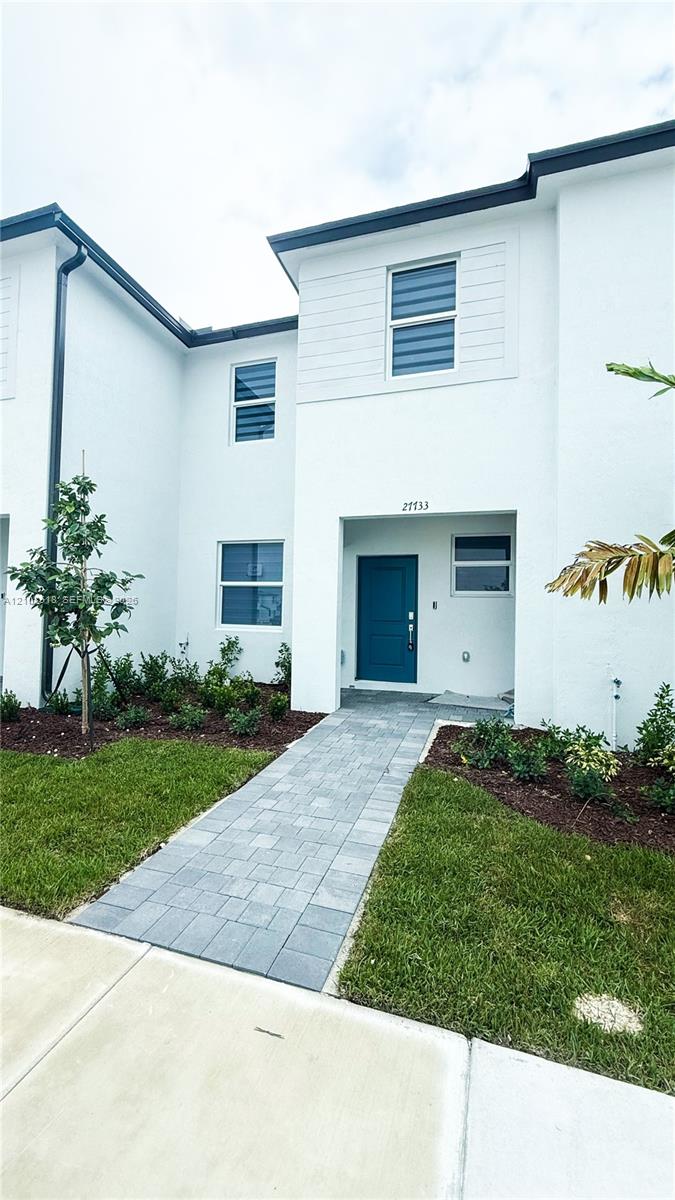 Contemporary exterior featuring a white smooth-stucco facade, a solid blue entry door, multi-pane windows, and a paved stone walkway