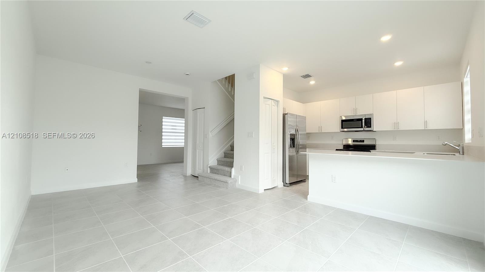 Open-concept kitchen featuring flat-panel white cabinetry, quartz countertops, stainless steel appliances, and large-format tile flooring