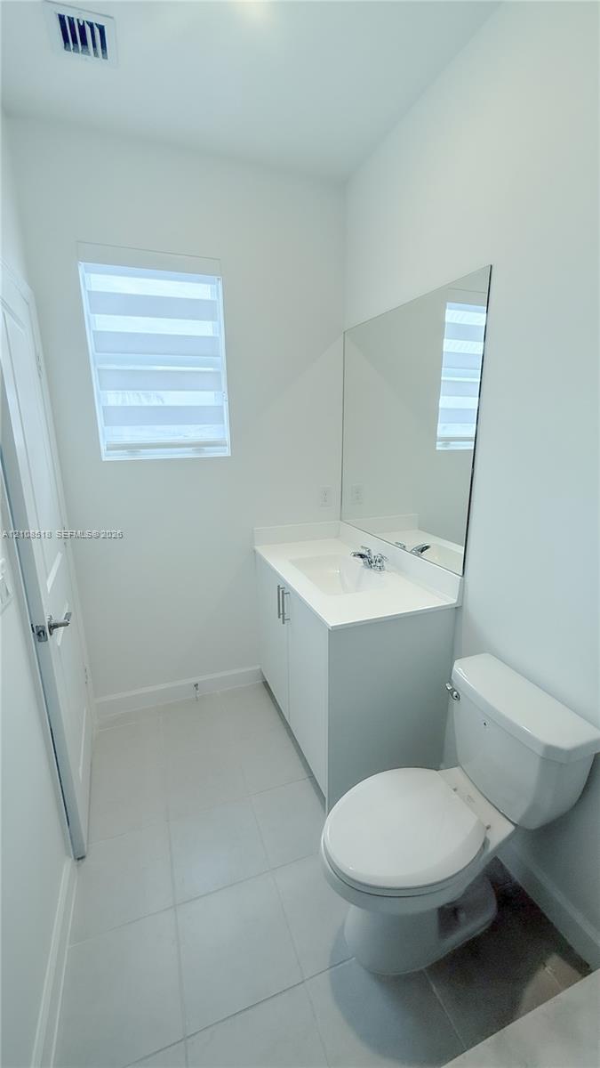 White vanity with an integrated countertop, large rectangular wall-mounted mirror, ceramic tile flooring, and layered light-filtering window treatments