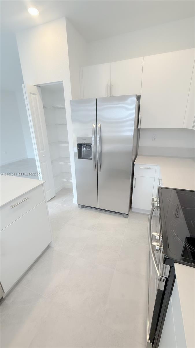 Kitchen featuring white cabinetry, light-toned stone-finish countertops, stainless steel appliances, and a walk-in pantry with built-in shelving