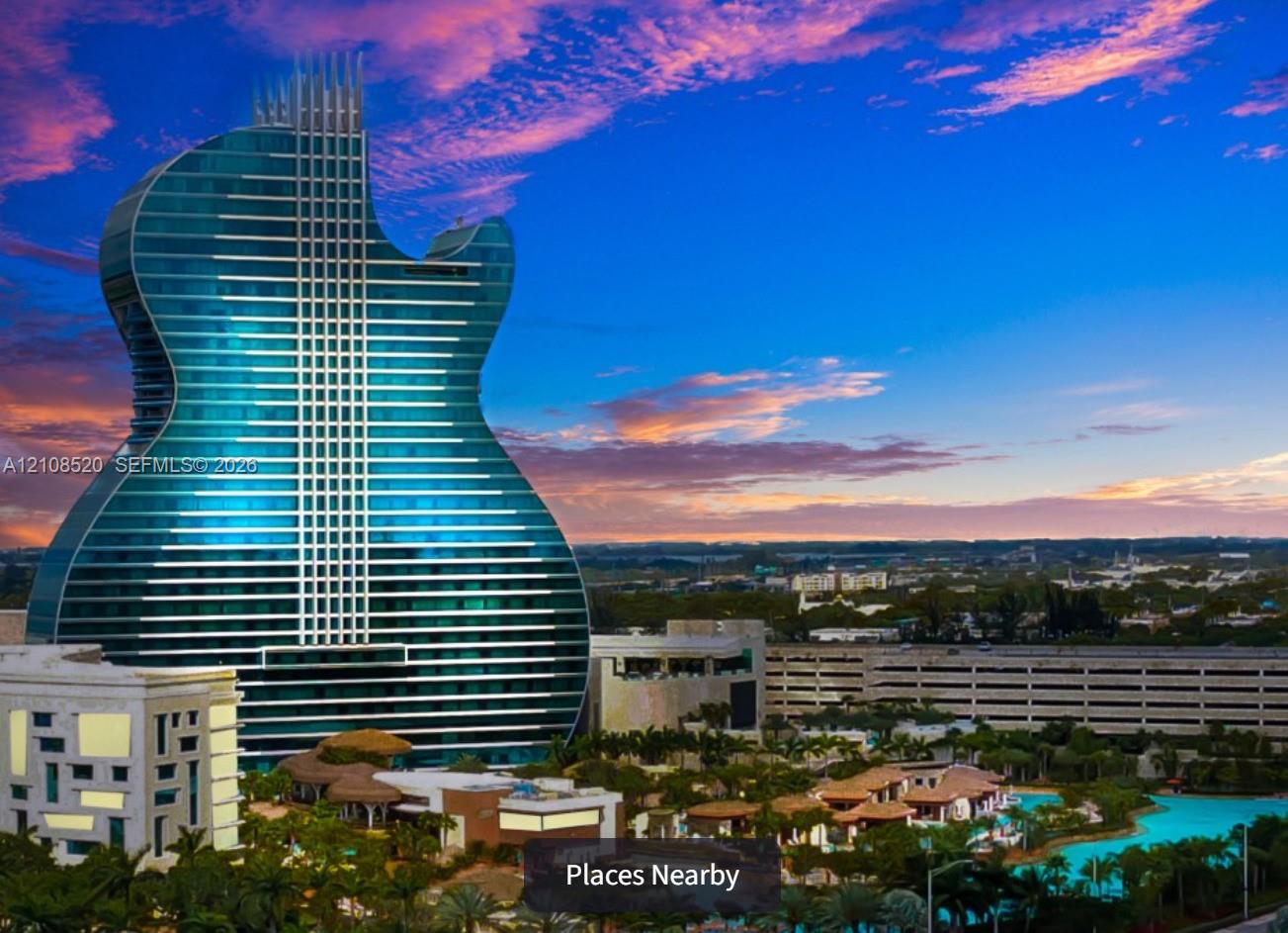 Iconic guitar-shaped high-rise structure featuring a glass-paneled exterior, expansive swimming pool, tropical landscaping, and multi-level parking facility