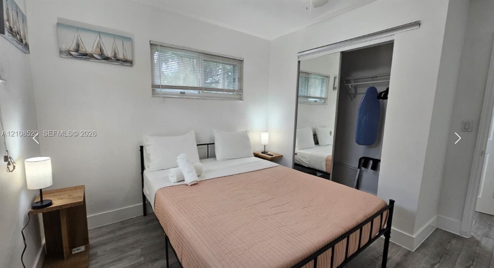 Room featuring wood-finish flooring, sliding mirror-door closet with integrated shelving, and a horizontal sliding window Room featuring wood-finish flooring, sliding mirror-door closet with integrated shelving, and a horizontal sliding window