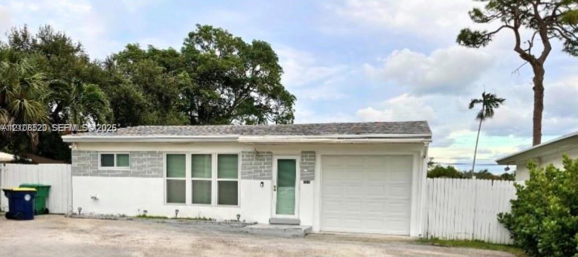 Single-story exterior featuring white stucco finish, decorative stone veneer accents, an attached one-car garage, and a white picket fence