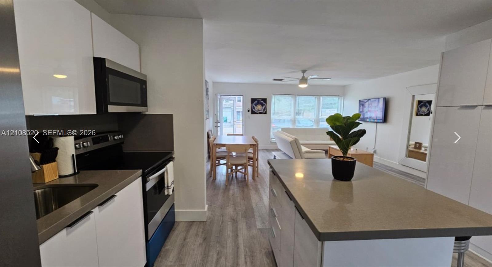 Kitchen featuring white gloss cabinetry, stone-finish countertops, stainless steel appliances, a central island, and wood-finish flooring Kitchen featuring white gloss cabinetry, stone-finish countertops, stainless steel appliances, a central island, and wood-finish flooring