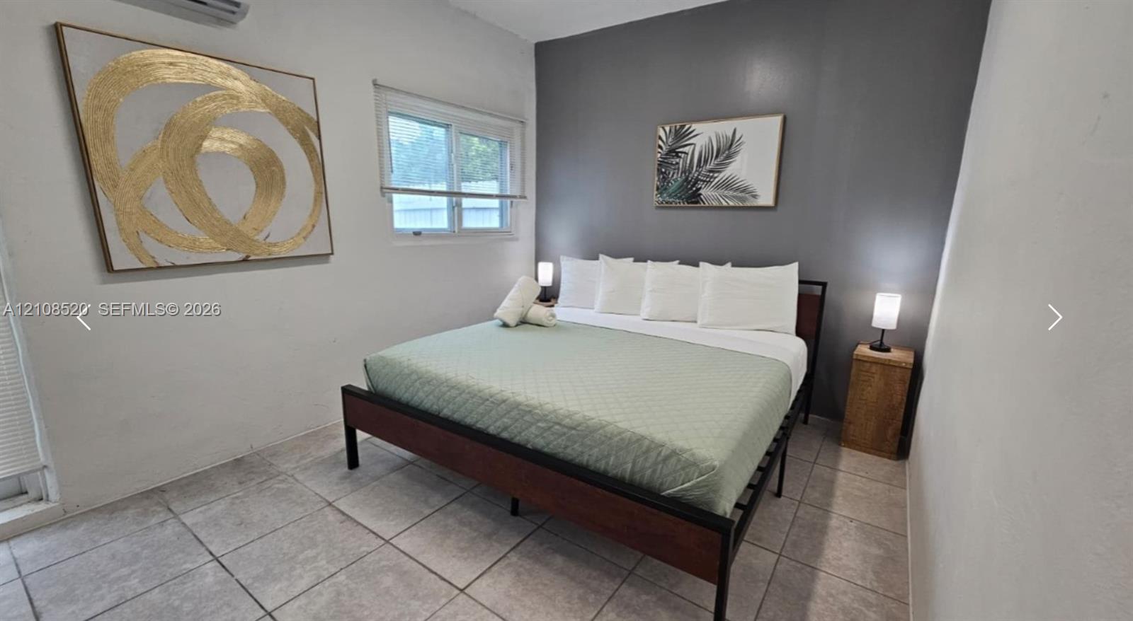 Room featuring tile flooring, a charcoal accent wall, and a wall-mounted climate control unit Room featuring tile flooring, a charcoal accent wall, and a wall-mounted climate control unit