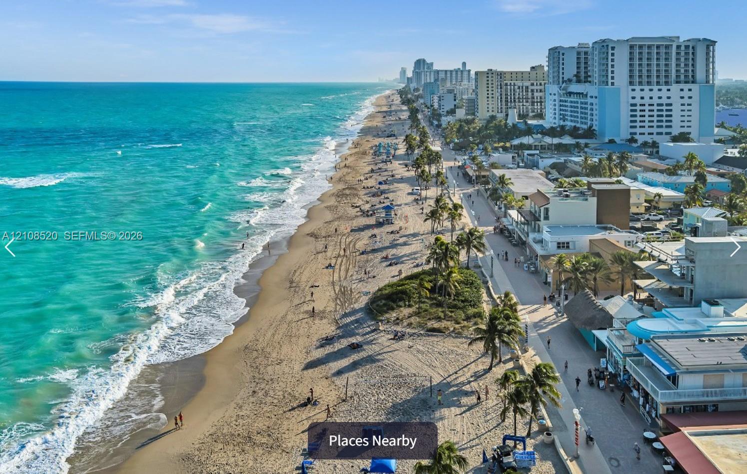 Aerial perspective of an expansive sandy coastline featuring turquoise ocean waters and established palm tree landscaping