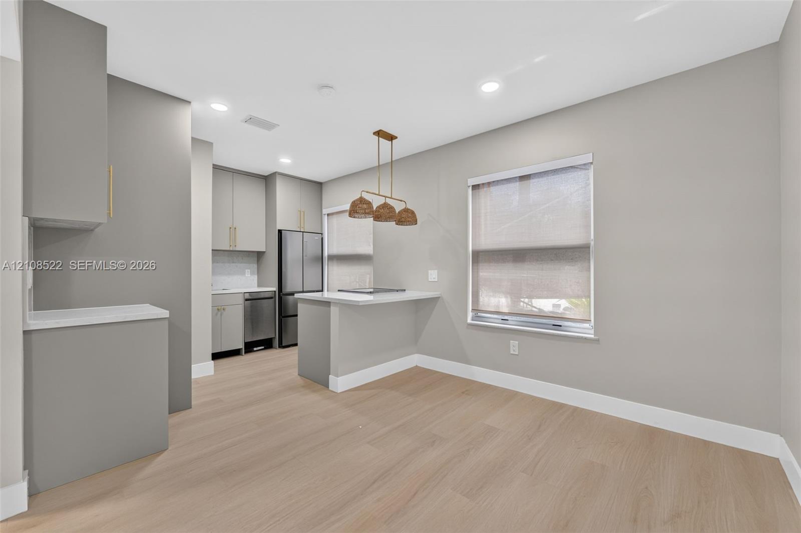 Kitchen featuring wood-finish flooring, matte-finish cabinetry, stone-surfaced countertops, stainless steel appliances, and multi-pendant overhead lighting