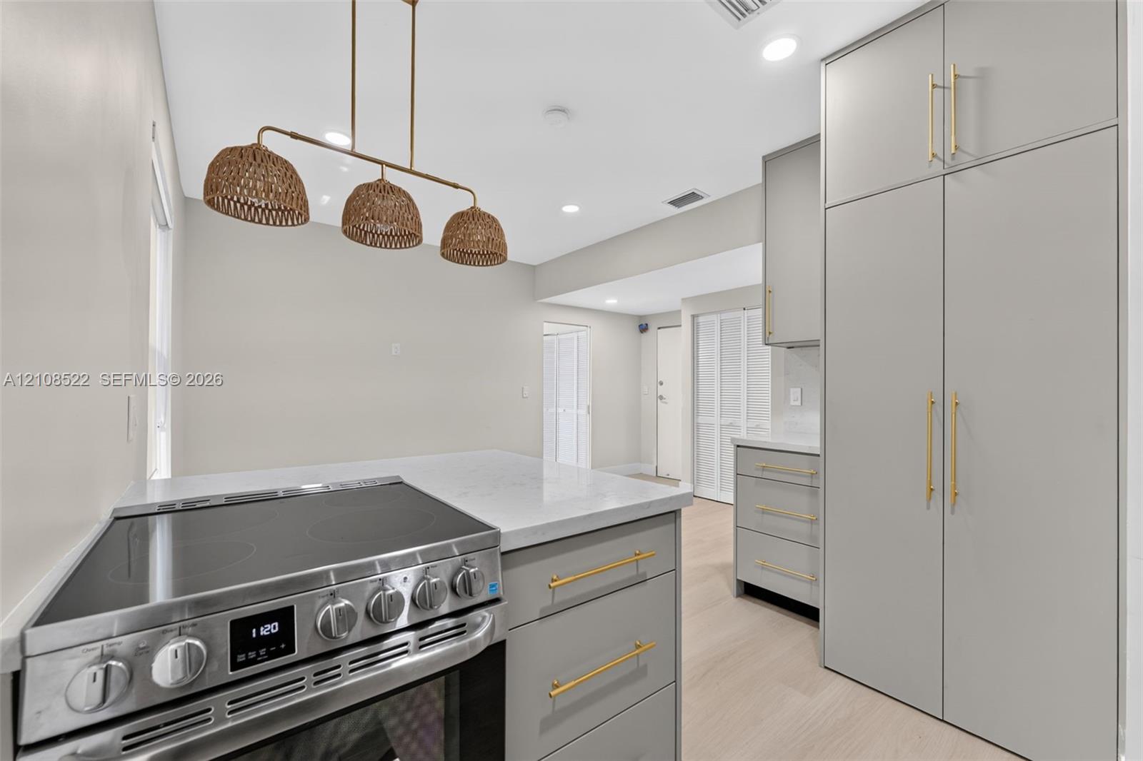 Kitchen featuring matte gray cabinetry with gold-toned hardware, quartz countertops, a stainless steel electric range, and a triple-pendant woven light fixture over wood-finish flooring