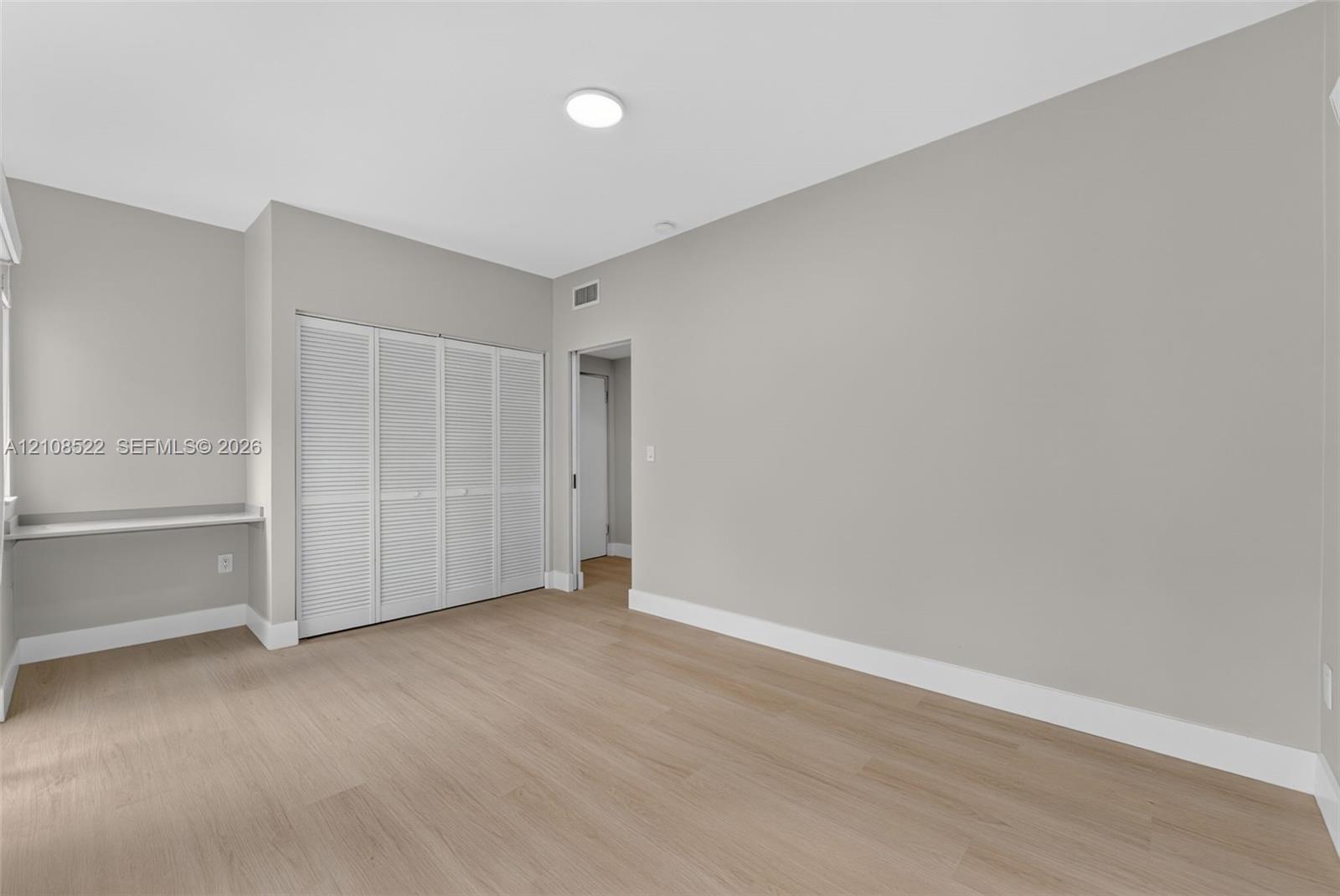 Room featuring wood-finish flooring, neutral wall paint, a built-in wall desk, and a four-panel louvered closet door