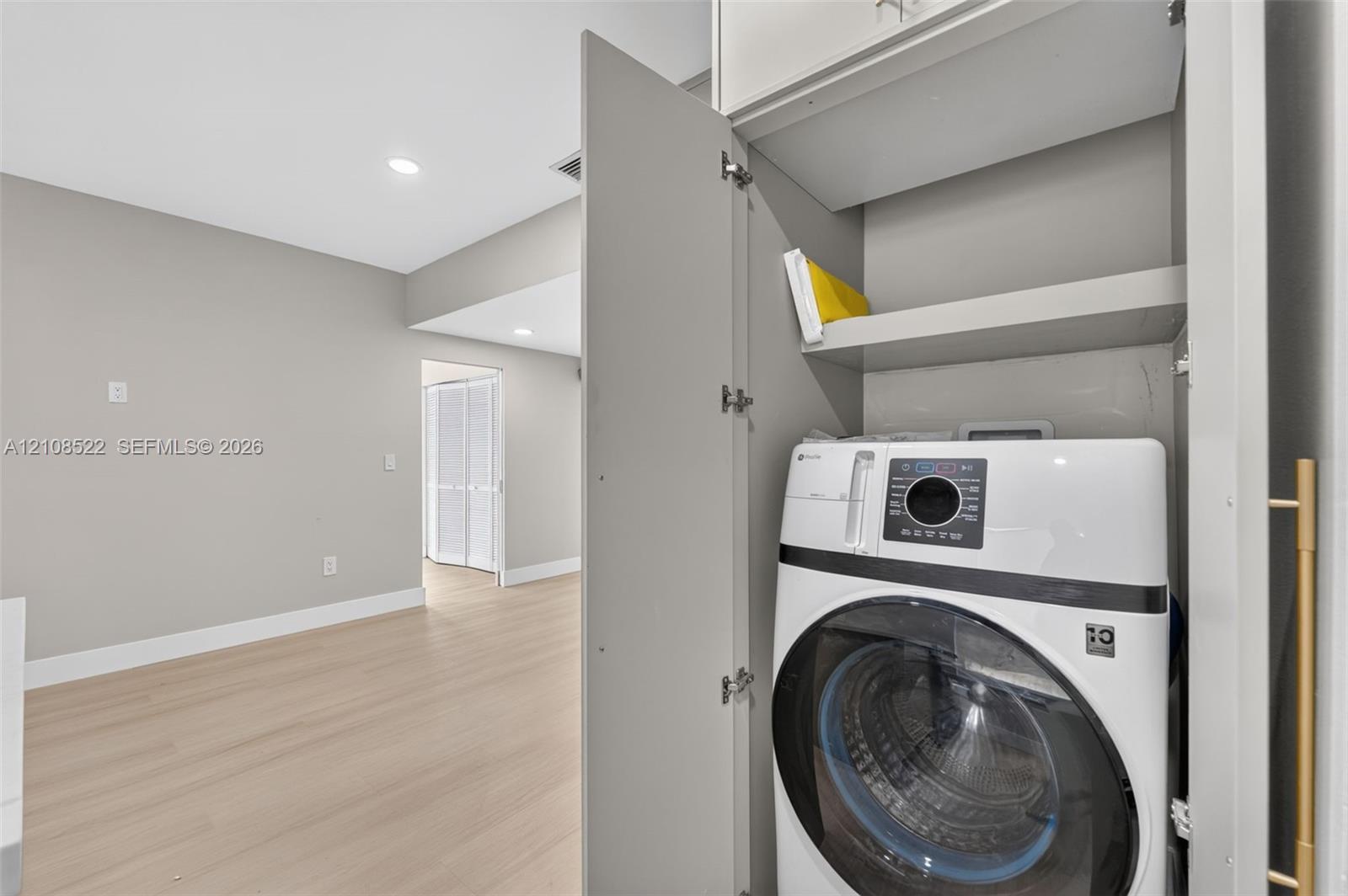 Laundry closet featuring built-in cabinetry, overhead shelving, and light wood-finish flooring