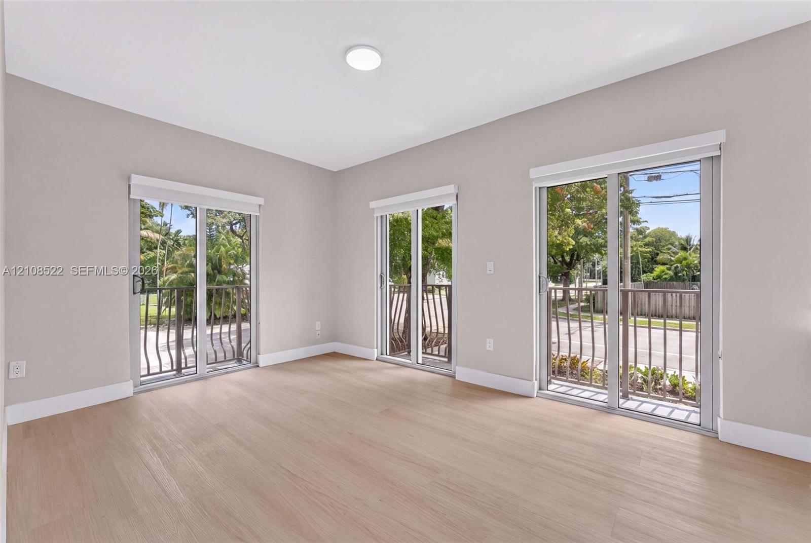Neutral-toned interior featuring wood-finish flooring, three sliding glass doors, and metal railings