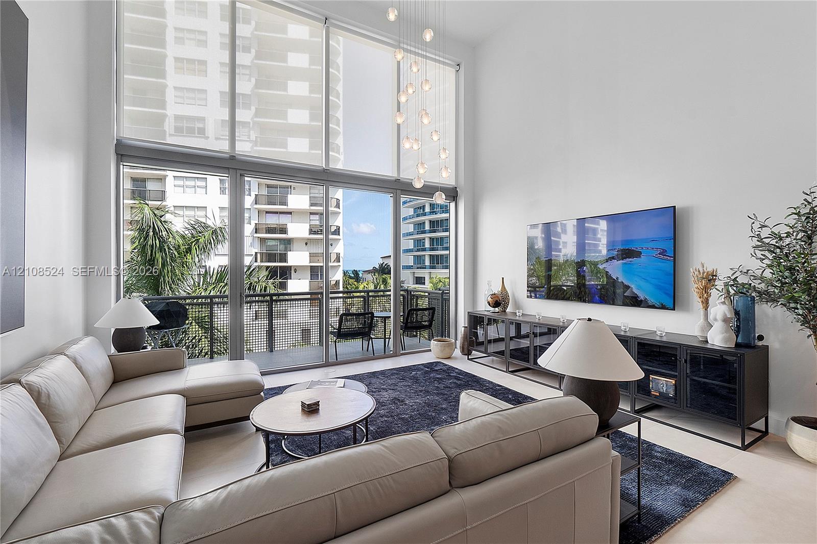 Double-height ceilings, floor-to-ceiling glass windows, recessed lighting, and a private balcony with a metal railing
