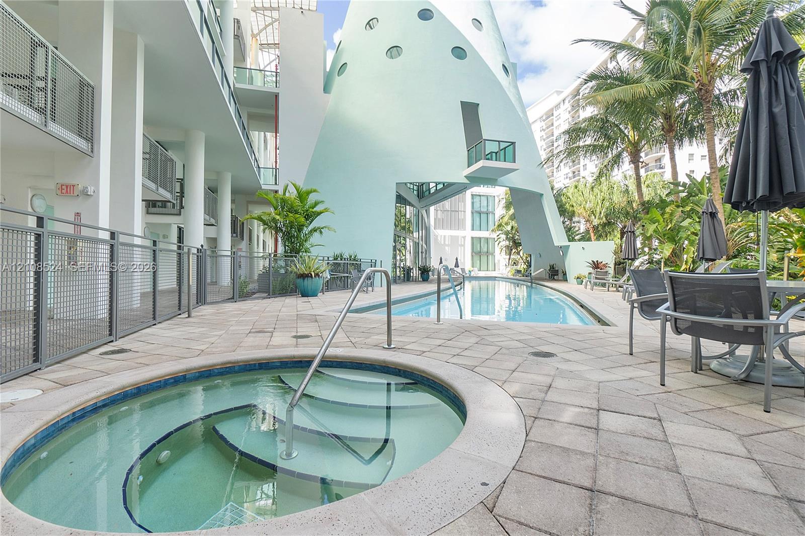Outdoor pool area featuring a recessed circular spa with metal handrails, a paved stone deck, and a distinctive multi-level architectural structure