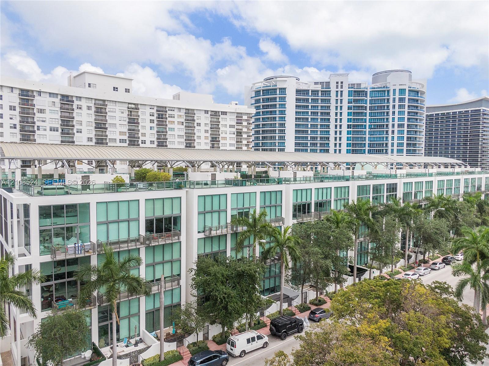 Multi-story residential building featuring floor-to-ceiling glass windows, private balconies, and an expansive rooftop terrace with a metal canopy structure