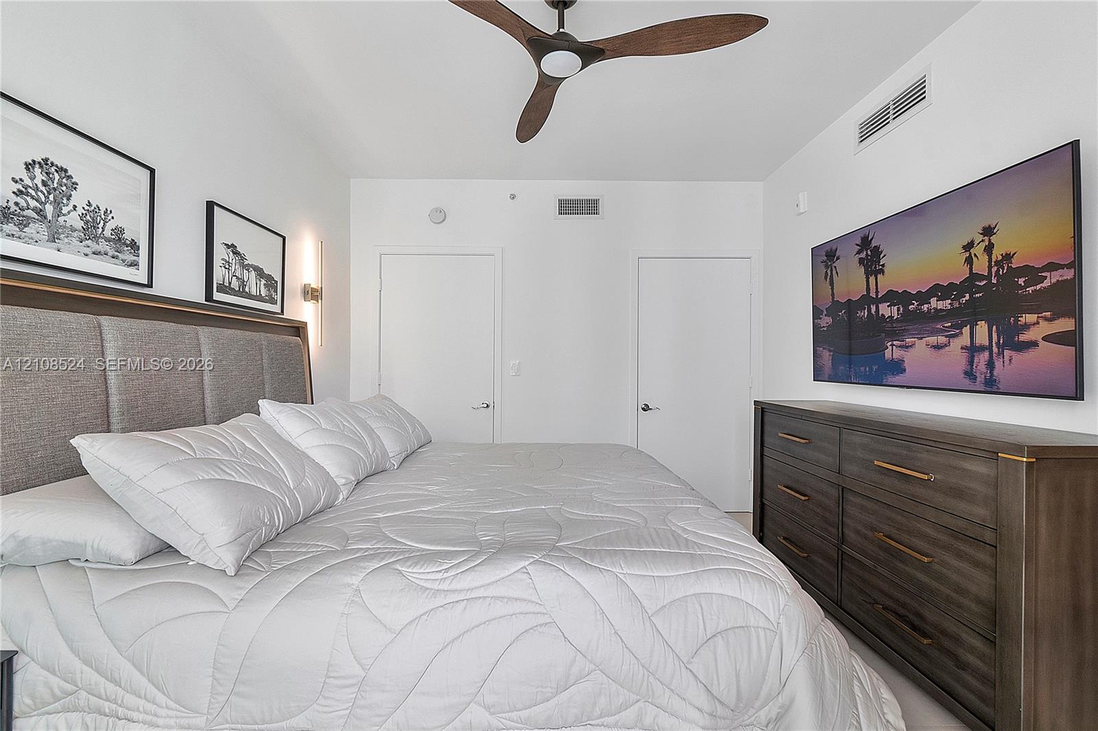 Bedroom featuring a floor-to-ceiling upholstered headboard, multi-blade ceiling fan, and solid-core interior doors Bedroom featuring a floor-to-ceiling upholstered headboard, multi-blade ceiling fan, and solid-core interior doors