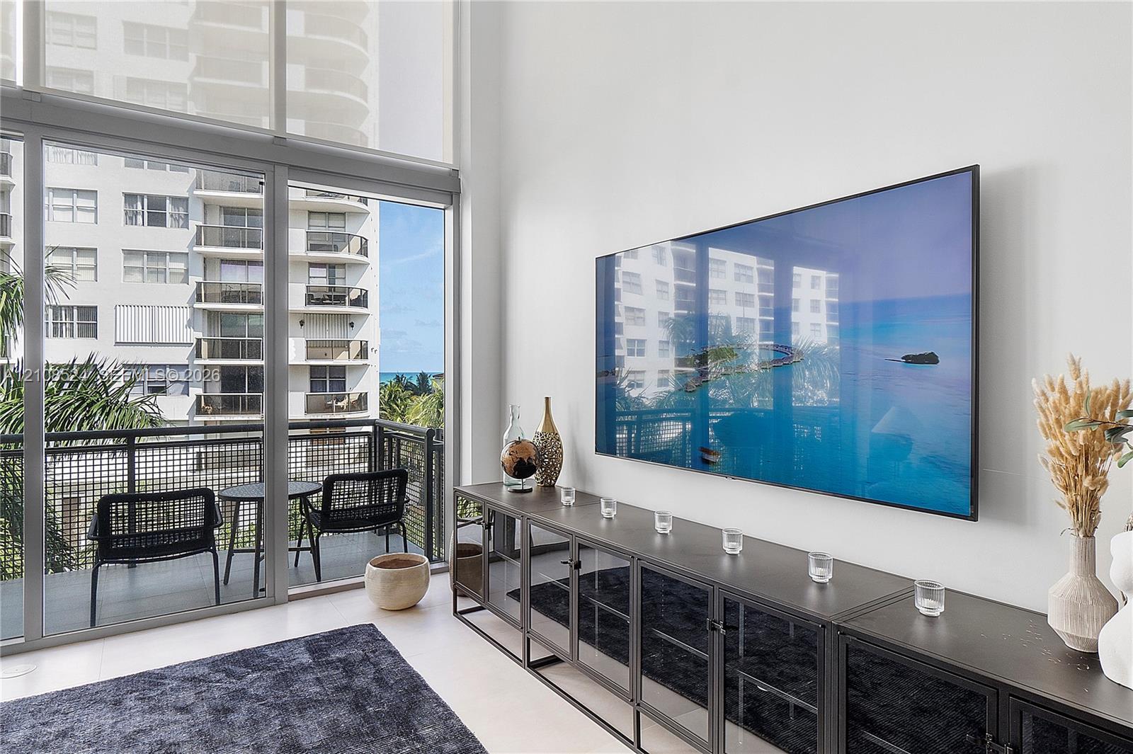 Floor-to-ceiling windows, double-height ceilings, and a private balcony with metal railings