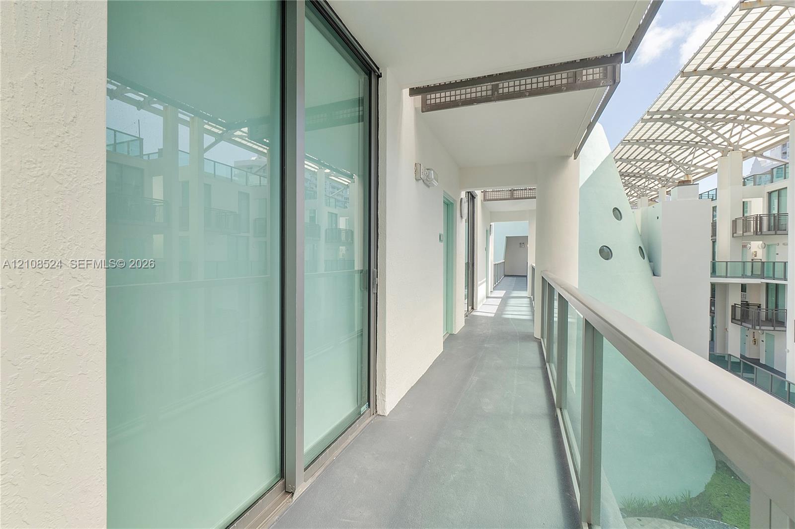 Covered balcony featuring full-height glass sliding doors, smooth concrete flooring, and a glass-panel railing Covered balcony featuring full-height glass sliding doors, smooth concrete flooring, and a glass-panel railing