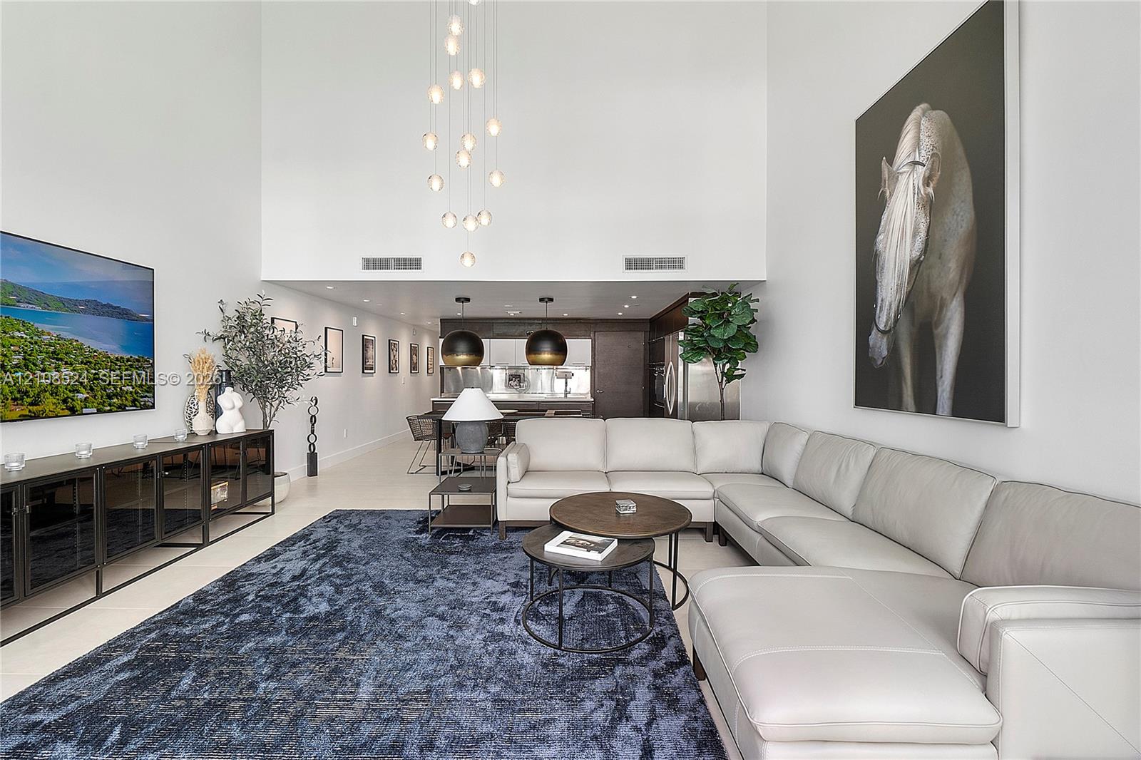 Expansive living area featuring double-height ceilings, floor-to-ceiling wall space, custom multi-tiered pendant lighting, and sleek dark-finish cabinetry