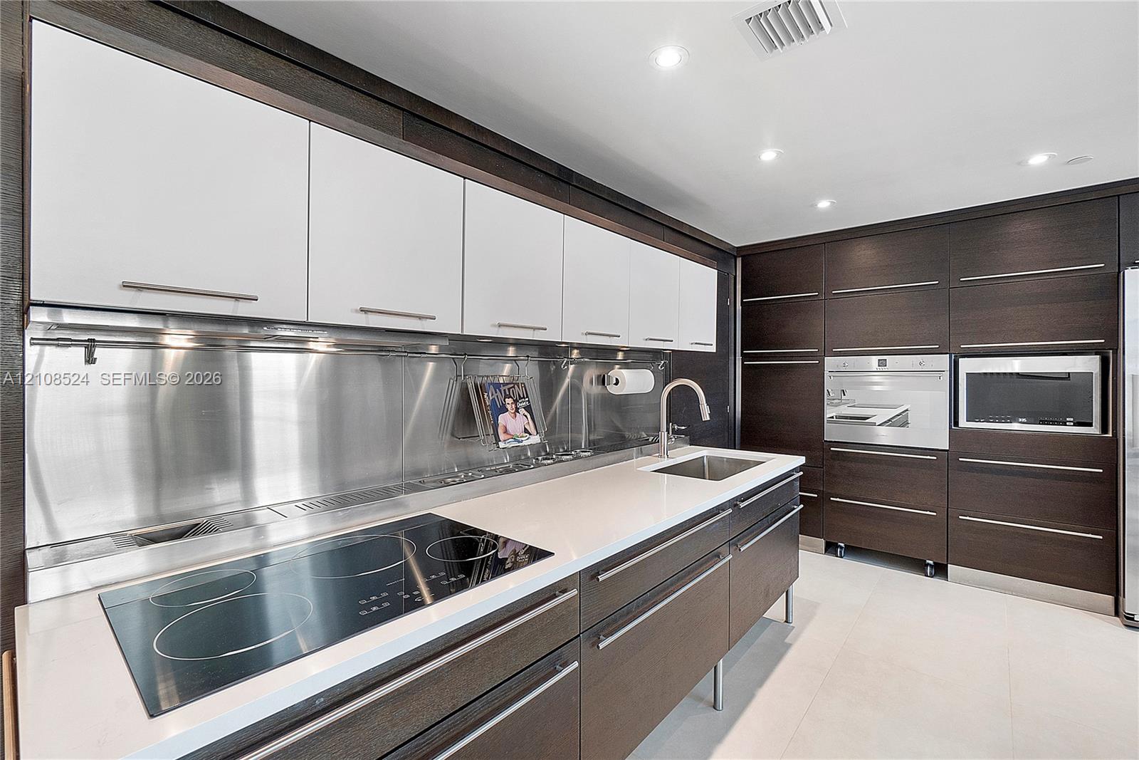 Kitchen featuring white upper cabinetry, dark wood-finish lower cabinetry, metallic backsplash, stone countertops, and built-in stainless steel appliances